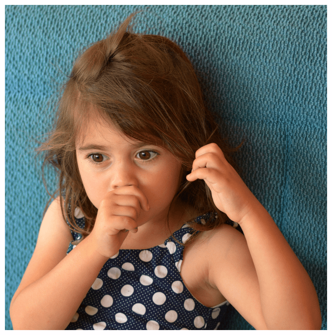 Little girl with dark hair and eyes, sucking her thumb and playing with hair hair with the other hand