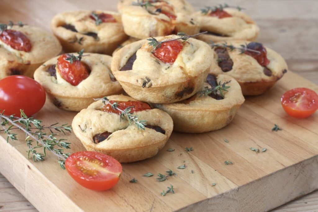 mini toads in the hole stacked on a wooden board with tomatoes and thyme to garnish