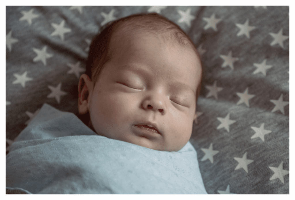 Sleeping baby in darkened room. The baby is swaddles to he can't use his hands to scratch his eczema.