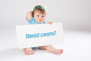 Toddler girl scratching her neck with one hand and holding a sign asking Steriods? in the other